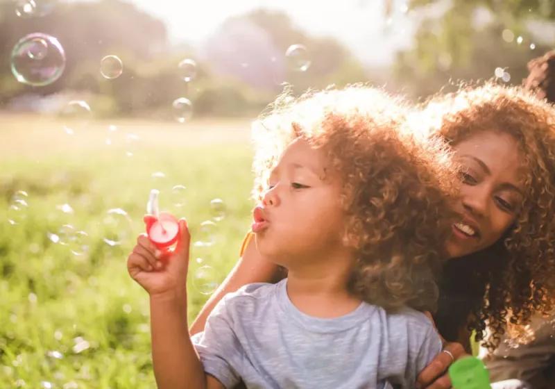 Picture of a child blowing bubbles with smiling mother behind