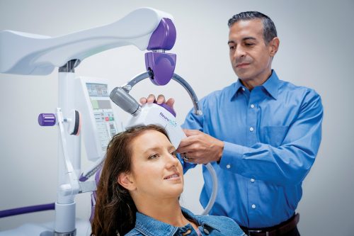 Image of patient sitting in a NeuroStar chair with physician positioning the wand on her head